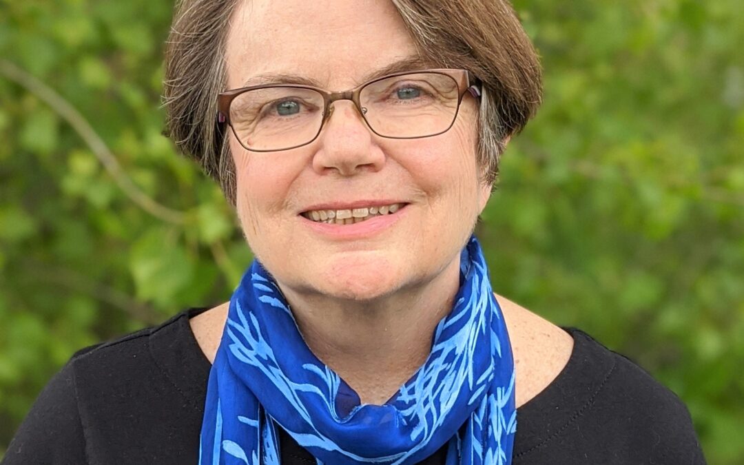 Rev. Diane Dowgiert is middle aged with short brown hair, wearing glasses, a black top and a blue scarf.
